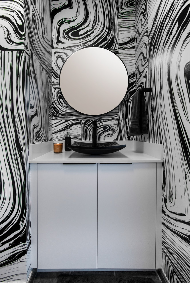 Photo of a contemporary powder room in Miami with flat-panel cabinets, white cabinets, multi-coloured walls, a vessel sink, black floor and white benchtops.