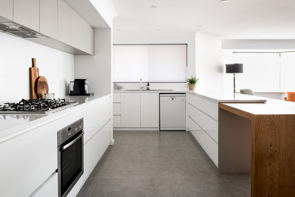 Photo of a large modern galley open plan kitchen in Perth with a drop-in sink, flat-panel cabinets, white cabinets, quartz benchtops, white splashback, porcelain splashback, stainless steel appliances, porcelain floors, with island and brown floor.