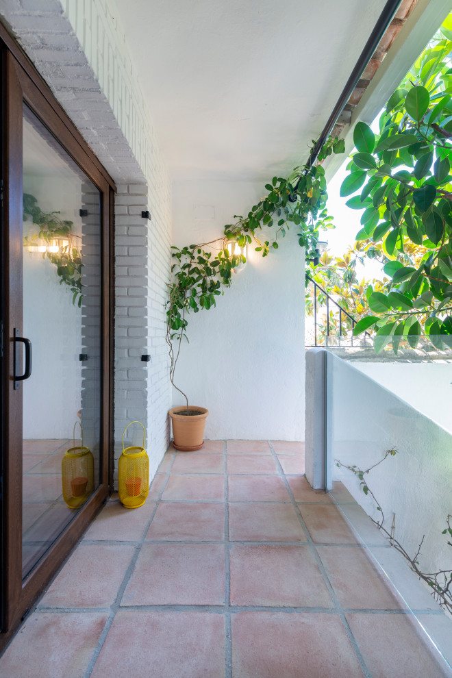 Свежая идея для дизайна: маленькая веранда на боковом дворе в средиземноморском стиле с растениями в контейнерах, покрытием из плитки, защитой от солнца и стеклянными перилами для на участке и в саду - отличное фото интерьера
