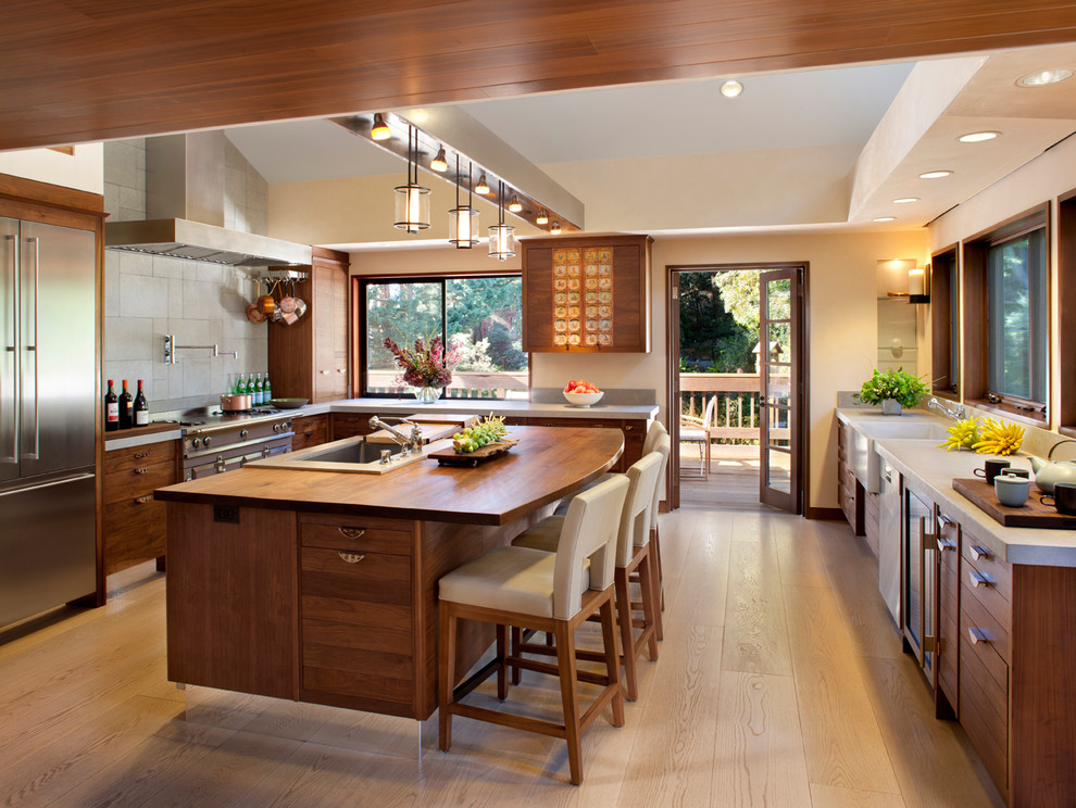 Inspiration for a large transitional kitchen in San Francisco with stainless steel appliances, wood benchtops, a drop-in sink, flat-panel cabinets, medium wood cabinets, grey splashback, cement tile splashback, light hardwood floors, with island and brown floor.