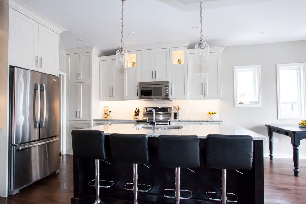 Example of a large transitional u-shaped dark wood floor and brown floor eat-in kitchen design in Toronto with an undermount sink, shaker cabinets, white cabinets, quartz countertops, white backsplash, subway tile backsplash, stainless steel appliances, an island and white countertops