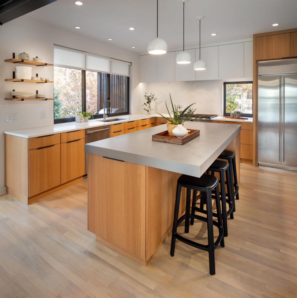 Photo of a large contemporary l-shaped eat-in kitchen in DC Metro with an undermount sink, flat-panel cabinets, light wood cabinets, quartz benchtops, white splashback, stone slab splashback, stainless steel appliances, light hardwood floors, with island, brown floor and grey benchtop.