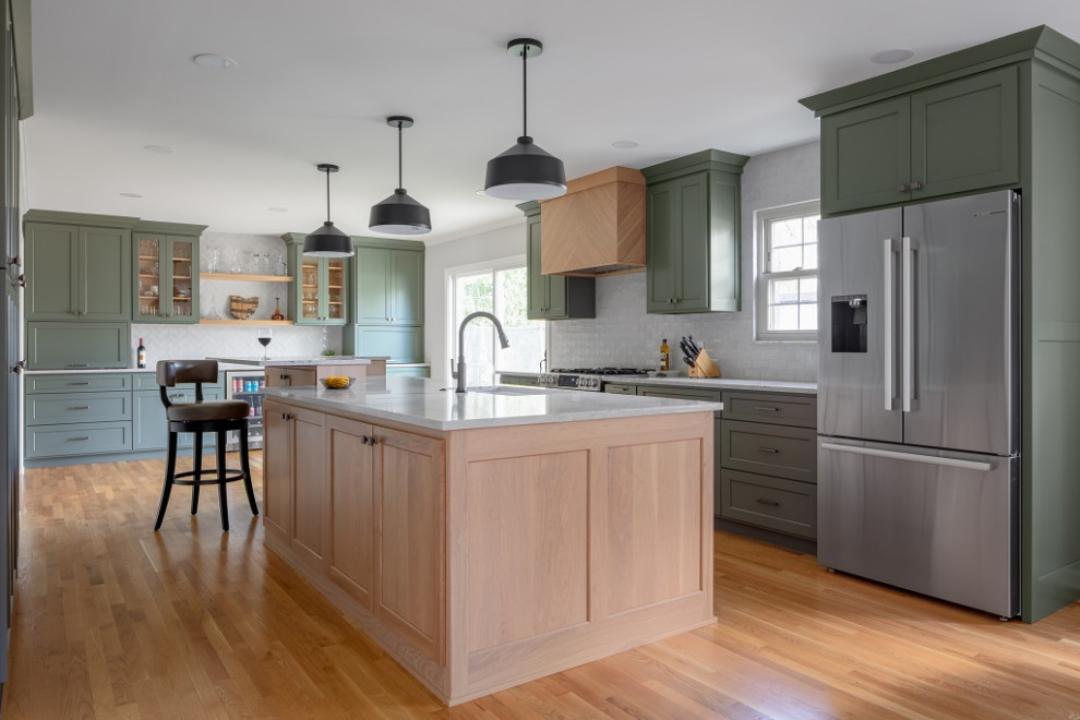 Large traditional galley kitchen/diner in Columbus with a submerged sink, shaker cabinets, green cabinets, engineered stone countertops, grey splashback, ceramic splashback, stainless steel appliances, light hardwood flooring, an island, brown floors and white worktops.