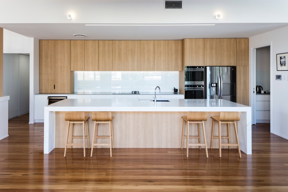 Inspiration for a contemporary galley open plan kitchen in Sunshine Coast with a drop-in sink, flat-panel cabinets, light wood cabinets, white splashback, glass sheet splashback, stainless steel appliances, medium hardwood floors, with island and brown floor.