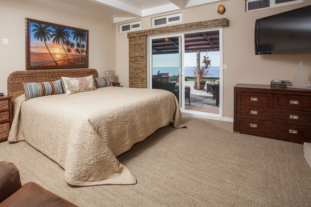 This is an example of a large beach style master bedroom in Orange County with beige walls, carpet, beige floor, a standard fireplace and a brick fireplace surround.