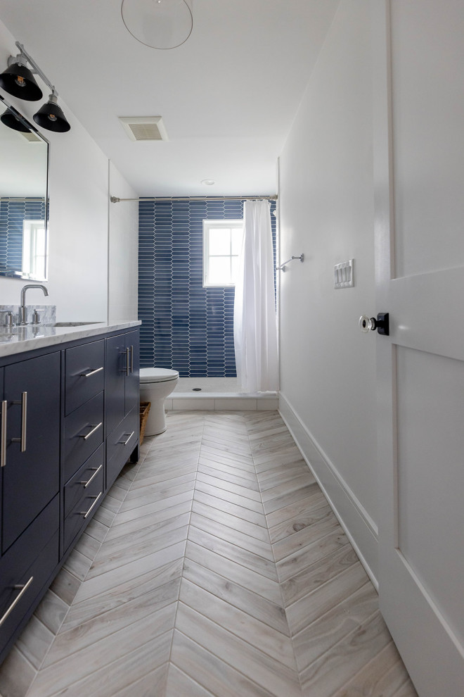 Cette image montre une salle de bain marine de taille moyenne avec WC à poser, un mur blanc, un sol en carrelage imitation parquet, un placard à porte plane, des portes de placard bleues, un carrelage bleu, des carreaux de céramique, un lavabo encastré, un plan de toilette en marbre, un sol beige, une cabine de douche avec un rideau, un plan de toilette blanc, meuble double vasque et meuble-lavabo sur pied.