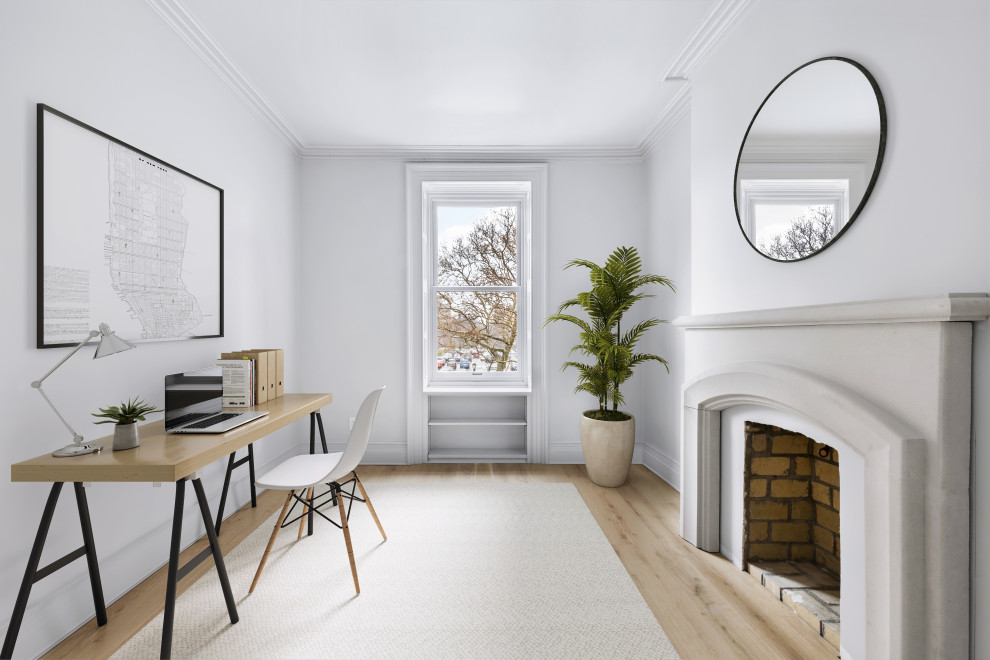 Photo of a mid-sized transitional home studio in New York with grey walls, light hardwood floors, a standard fireplace, a concrete fireplace surround, a freestanding desk and beige floor.