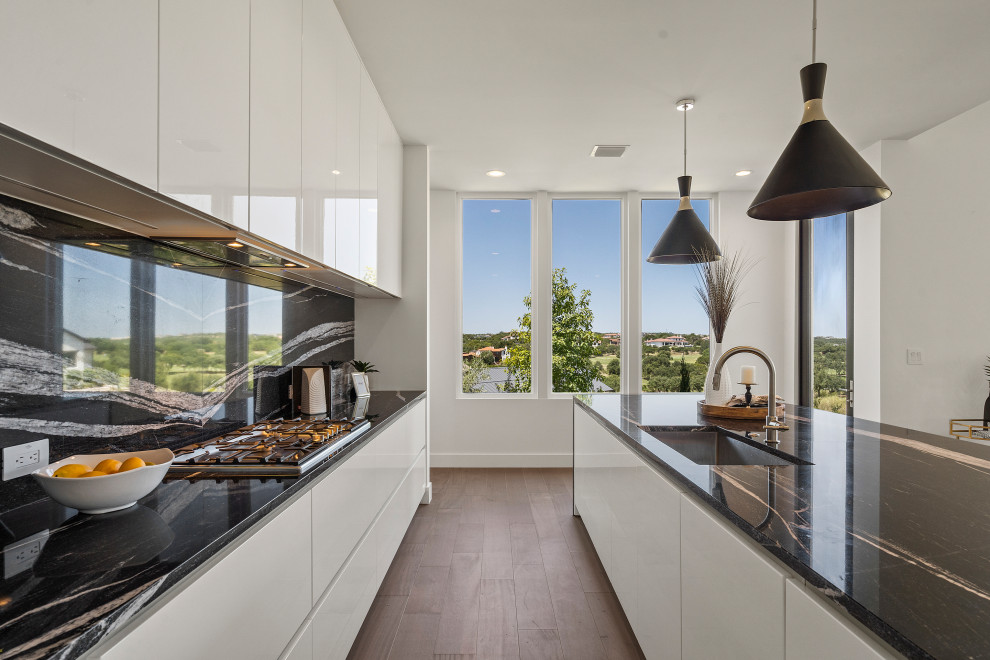 Design ideas for a mid-sized contemporary galley eat-in kitchen in Austin with an undermount sink, flat-panel cabinets, white cabinets, granite benchtops, black splashback, granite splashback, stainless steel appliances, medium hardwood floors, with island, brown floor and black benchtop.