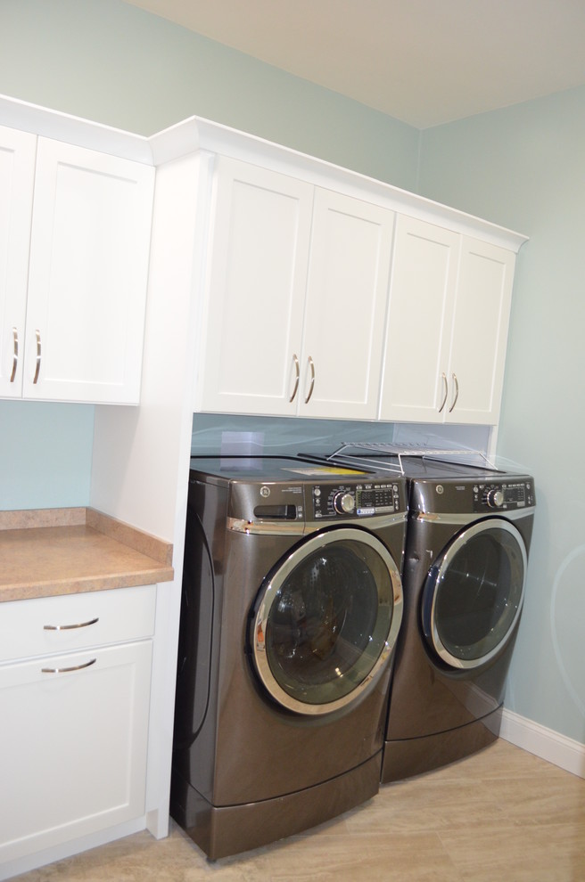 Photo of a large transitional dedicated laundry room in Boston with recessed-panel cabinets, white cabinets, laminate benchtops, blue walls, porcelain floors, a side-by-side washer and dryer and beige floor.
