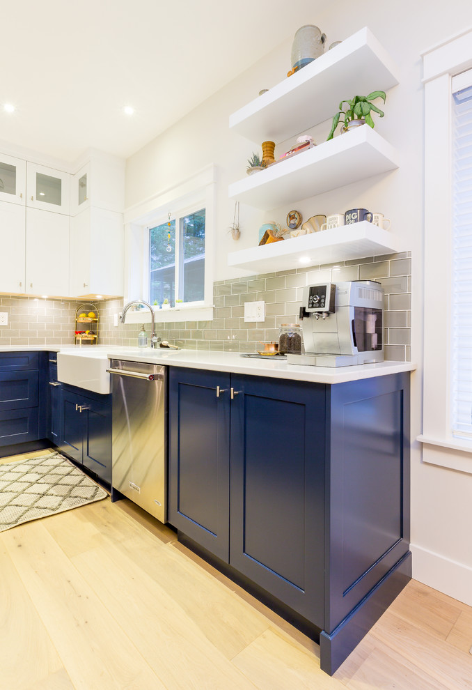 Example of a large transitional u-shaped light wood floor open concept kitchen design with a farmhouse sink, shaker cabinets, blue cabinets, quartz countertops, gray backsplash, glass tile backsplash, stainless steel appliances, an island and white countertops