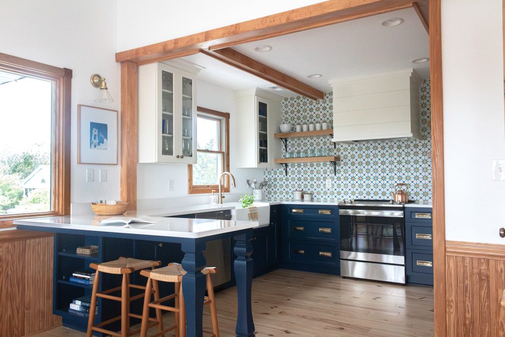 Inspiration for a medium sized beach style u-shaped kitchen/diner in Other with a belfast sink, flat-panel cabinets, blue cabinets, engineered stone countertops, blue splashback, cement tile splashback, stainless steel appliances, medium hardwood flooring, an island, white worktops and exposed beams.