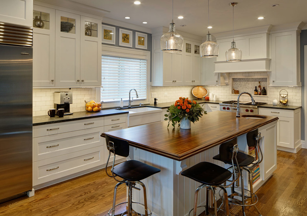 Mid-sized traditional l-shaped eat-in kitchen in Chicago with a farmhouse sink, shaker cabinets, white cabinets, wood benchtops, white splashback, subway tile splashback, stainless steel appliances, medium hardwood floors, with island and brown floor.