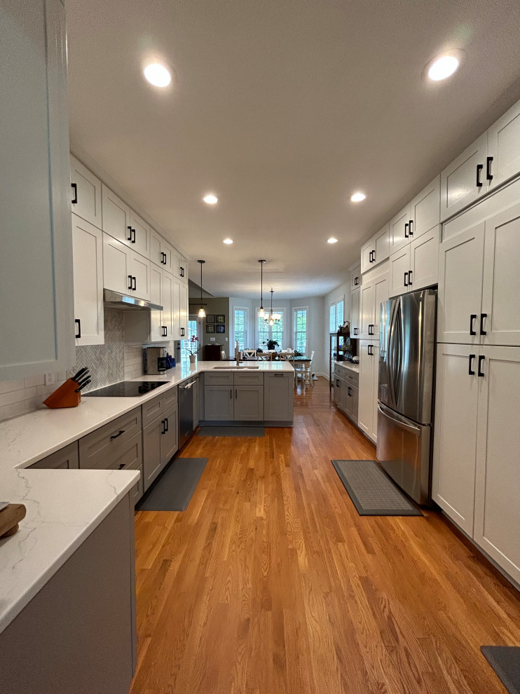 This is an example of a large transitional u-shaped eat-in kitchen in Raleigh with shaker cabinets, quartz benchtops and white splashback.