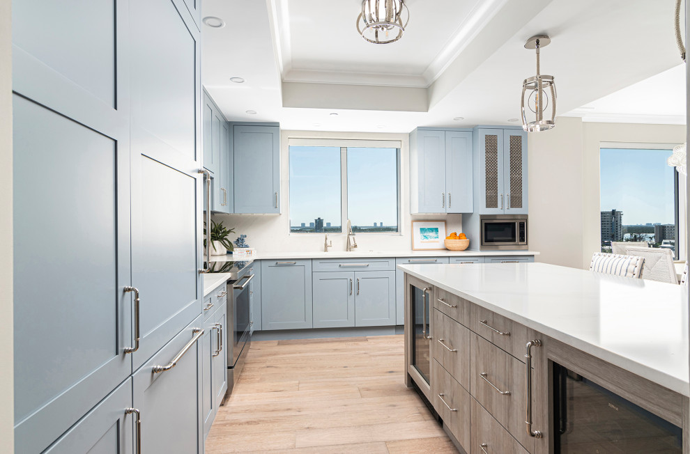 Mid-sized beach style l-shaped eat-in kitchen in Miami with an undermount sink, shaker cabinets, blue cabinets, quartz benchtops, white splashback, engineered quartz splashback, stainless steel appliances, medium hardwood floors, with island, white benchtop and recessed.