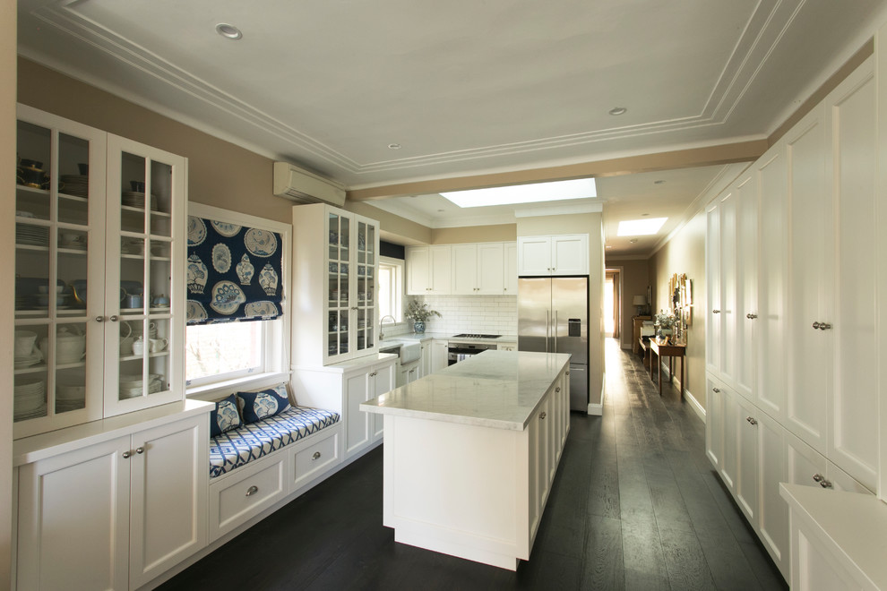 Inspiration for a transitional galley open plan kitchen in Sydney with a farmhouse sink, recessed-panel cabinets, white cabinets, quartz benchtops, white splashback, subway tile splashback, stainless steel appliances, dark hardwood floors, with island and white benchtop.