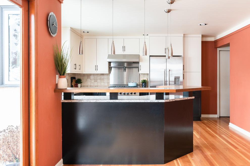 Example of a mid-sized transitional u-shaped medium tone wood floor and brown floor eat-in kitchen design with an undermount sink, shaker cabinets, distressed cabinets, quartz countertops, white backsplash, travertine backsplash, stainless steel appliances, a peninsula and multicolored countertops