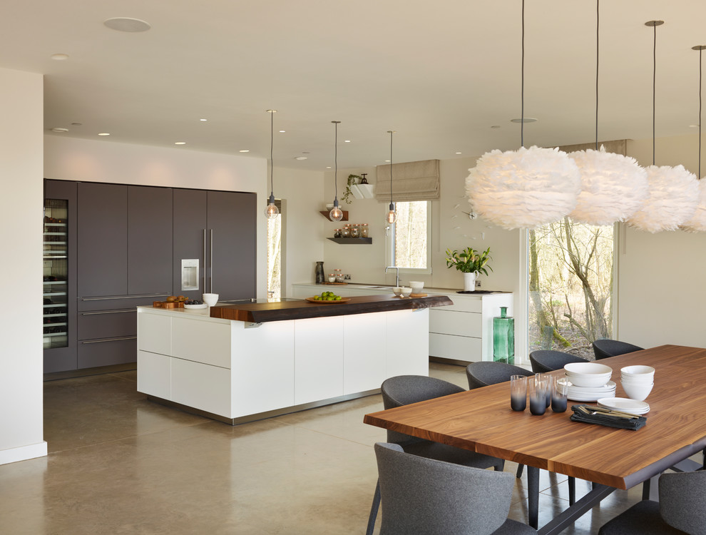 Design ideas for a large contemporary l-shaped open plan kitchen in Gloucestershire with a double-bowl sink, flat-panel cabinets, white cabinets, quartz benchtops, glass sheet splashback, stainless steel appliances, concrete floors and with island.