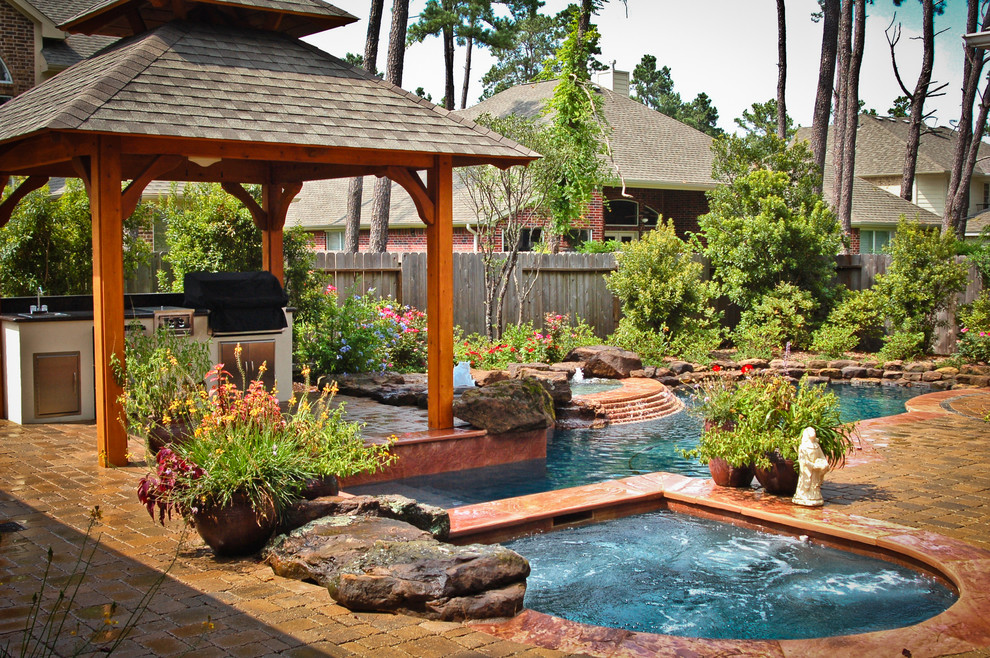Photo of a mid-sized mediterranean backyard custom-shaped natural pool in Houston with a hot tub and natural stone pavers.