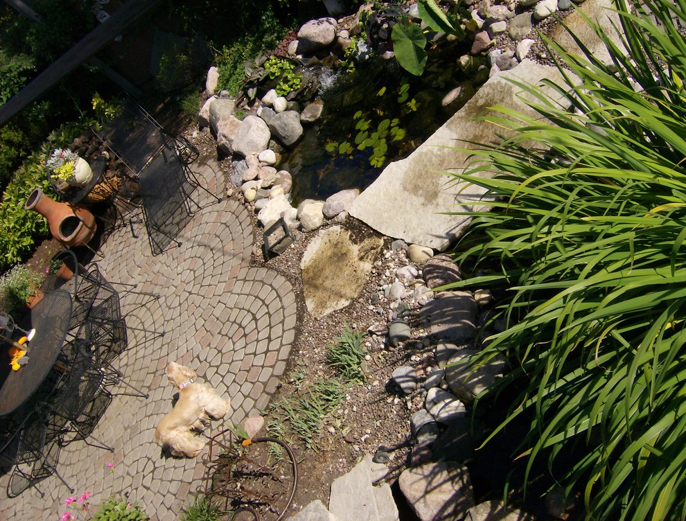 This is an example of a mid-sized eclectic backyard partial sun garden for summer in Chicago with a water feature and concrete pavers.