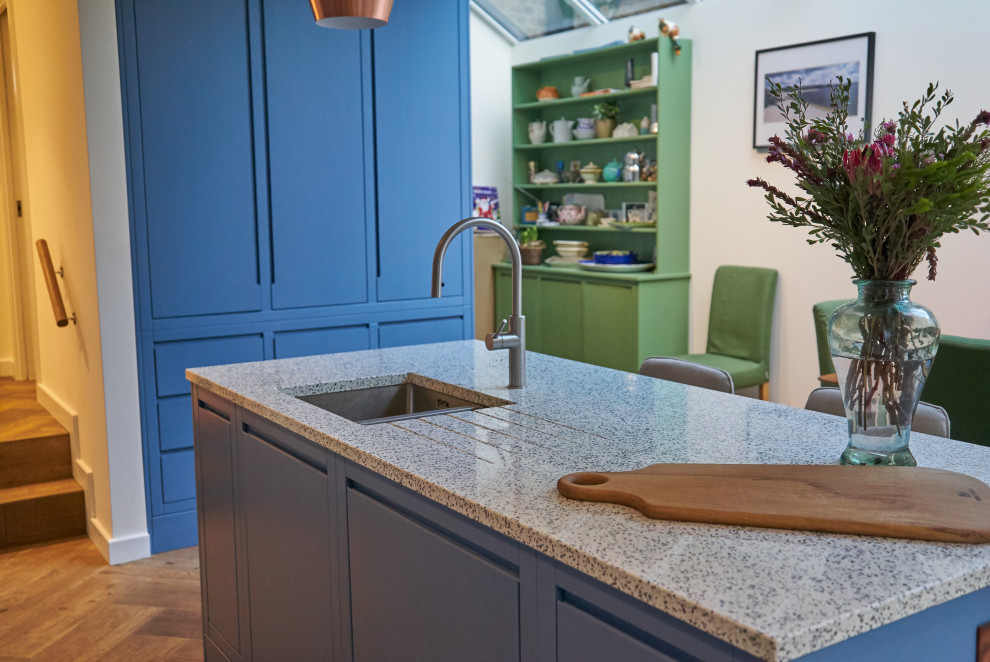 ロンドンにある高級な広いコンテンポラリースタイルのおしゃれなキッチン (一体型シンク、フラットパネル扉のキャビネット、青いキャビネット、再生ガラスカウンター、青いキッチンパネル、磁器タイルのキッチンパネル、白い調理設備、淡色無垢フローリング、青いキッチンカウンター、三角天井) の写真