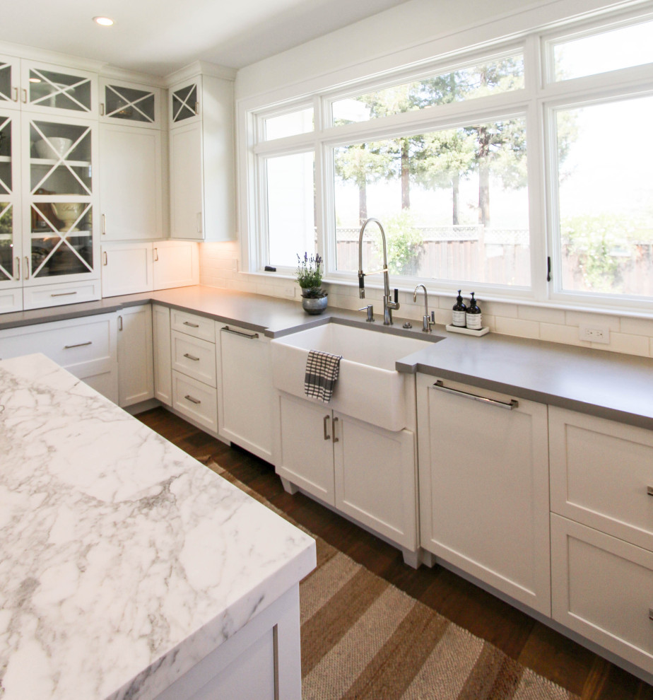 Inspiration for a large transitional u-shaped open plan kitchen in San Francisco with a farmhouse sink, shaker cabinets, white cabinets, quartz benchtops, white splashback, ceramic splashback, panelled appliances, medium hardwood floors, with island, brown floor and white benchtop.