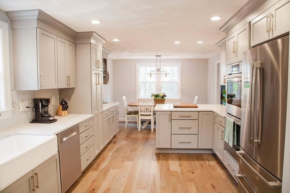 This is an example of a large transitional u-shaped eat-in kitchen in Boston with a farmhouse sink, recessed-panel cabinets, quartz benchtops, stainless steel appliances, medium hardwood floors, brown floor, grey cabinets, multi-coloured splashback, mosaic tile splashback and no island.