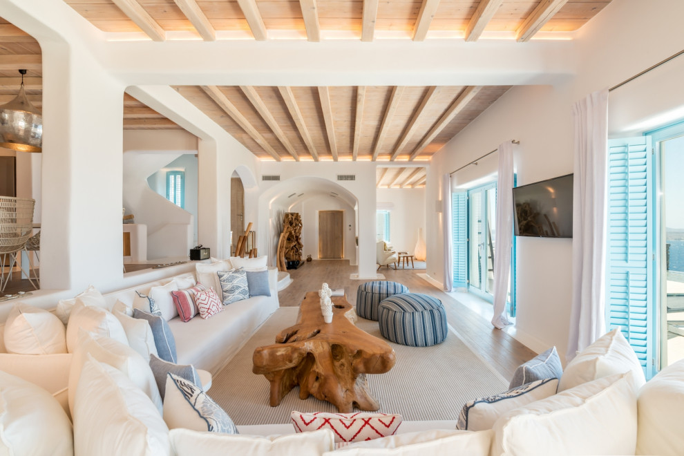 This is an example of a beach style open concept living room in Other with white walls, medium hardwood floors, a wall-mounted tv, brown floor, exposed beam and wood.