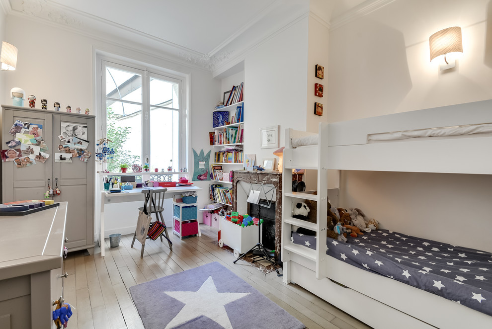 This is an example of a large transitional gender-neutral kids' bedroom for kids 4-10 years old in Paris with white walls and light hardwood floors.