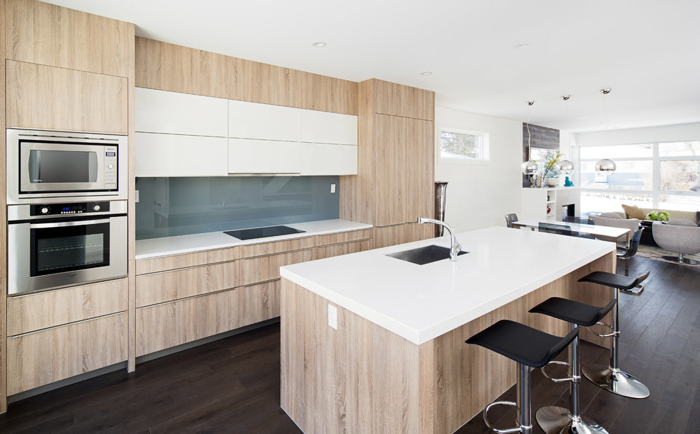Inspiration for a mid-sized modern single-wall eat-in kitchen in Calgary with an undermount sink, flat-panel cabinets, light wood cabinets, quartz benchtops, blue splashback, glass sheet splashback, panelled appliances, dark hardwood floors and with island.