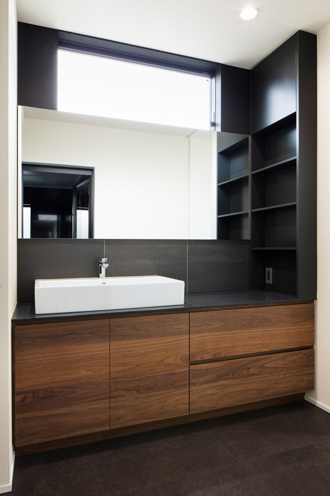 Стильный дизайн: туалет в стиле модернизм с темными деревянными фасадами, черной плиткой, настольной раковиной и черной столешницей - последний тренд