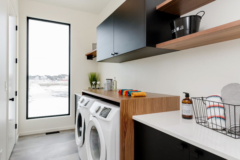 Large midcentury single-wall utility room in Other with flat-panel cabinets, black cabinets, ceramic floors, a side-by-side washer and dryer, grey floor, white benchtop and wood benchtops.