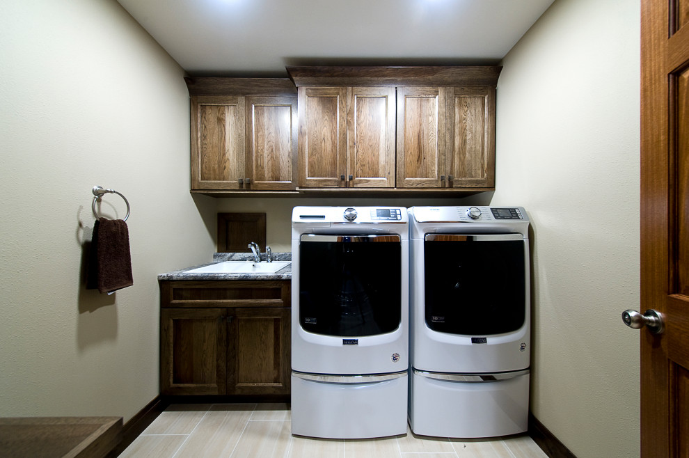 Modelo de cuarto de lavado lineal clásico de tamaño medio con fregadero bajoencimera, armarios con paneles lisos, puertas de armario marrones y lavadora y secadora juntas