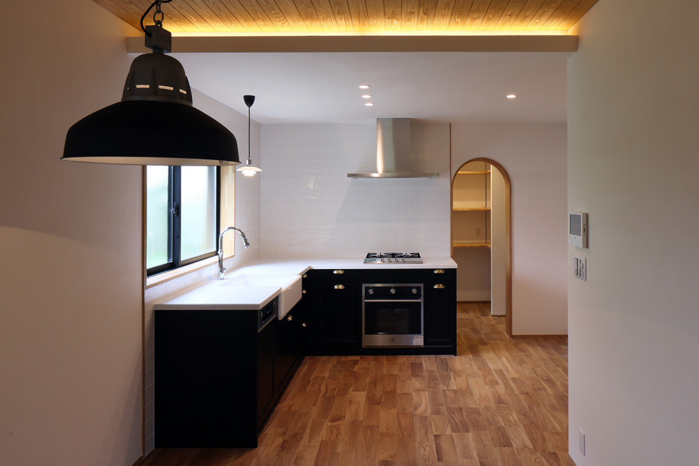 Foto på ett stort nordiskt vit kök, med en enkel diskho, svarta skåp, bänkskiva i koppar, vitt stänkskydd, stänkskydd i porslinskakel, integrerade vitvaror och mellanmörkt trägolv