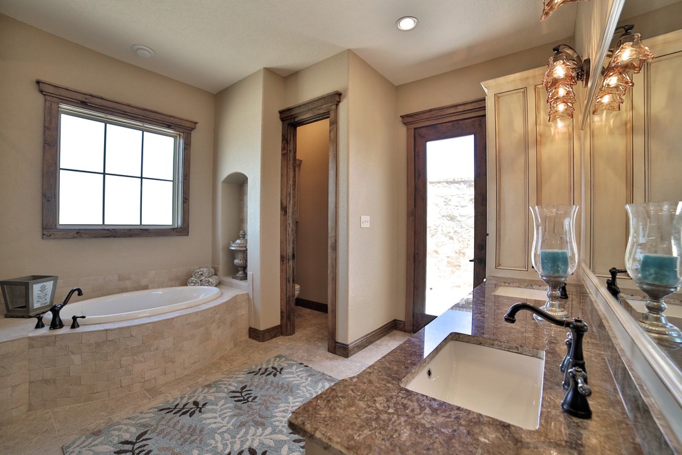 Design ideas for a mid-sized mediterranean master bathroom in Dallas with an undermount sink, shaker cabinets, granite benchtops, a drop-in tub, an alcove shower, a two-piece toilet, beige tile, stone tile, beige walls and porcelain floors.