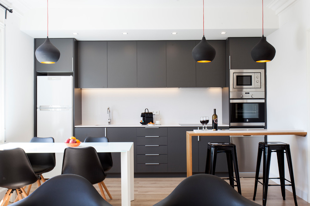 Design ideas for a mid-sized contemporary single-wall open plan kitchen in Barcelona with flat-panel cabinets, white splashback, stainless steel appliances, medium hardwood floors, a peninsula, black cabinets and brown floor.