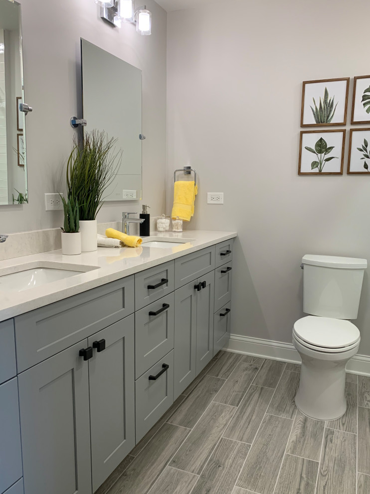 Photo of a mid-sized transitional kids bathroom in Chicago with shaker cabinets, grey cabinets, an alcove tub, a shower/bathtub combo, a two-piece toilet, white tile, ceramic tile, grey walls, ceramic floors, an undermount sink, engineered quartz benchtops, grey floor, a sliding shower screen, white benchtops, a niche, a double vanity and a built-in vanity.