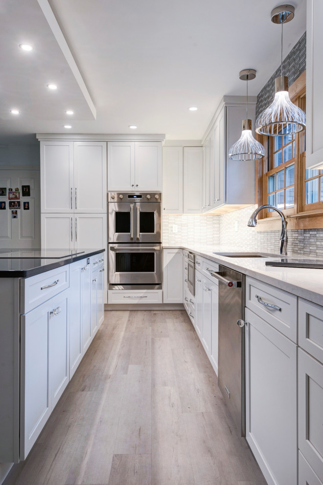 Example of a large transitional u-shaped light wood floor and beige floor open concept kitchen design in New York with an undermount sink, shaker cabinets, white cabinets, quartzite countertops, white backsplash, ceramic backsplash, stainless steel appliances, an island and white countertops