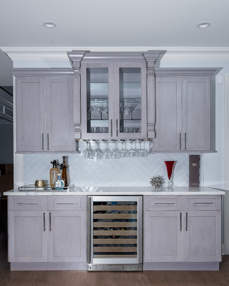 Design ideas for a mid-sized transitional single-wall wet bar in New York with grey cabinets, medium hardwood floors, shaker cabinets, marble benchtops, white splashback, glass tile splashback and brown floor.