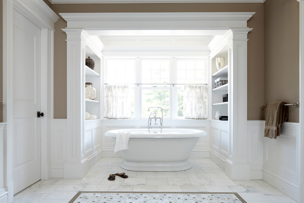 This is an example of a large traditional master bathroom in New York with a freestanding tub, brown walls, open cabinets, white cabinets, white tile, marble floors and white floor.