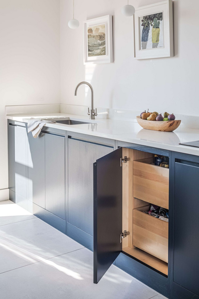 This is an example of a mid-sized contemporary l-shaped eat-in kitchen in Gloucestershire with a drop-in sink, flat-panel cabinets, blue cabinets, quartzite benchtops, white splashback, black appliances, ceramic floors, no island, white floor and white benchtop.
