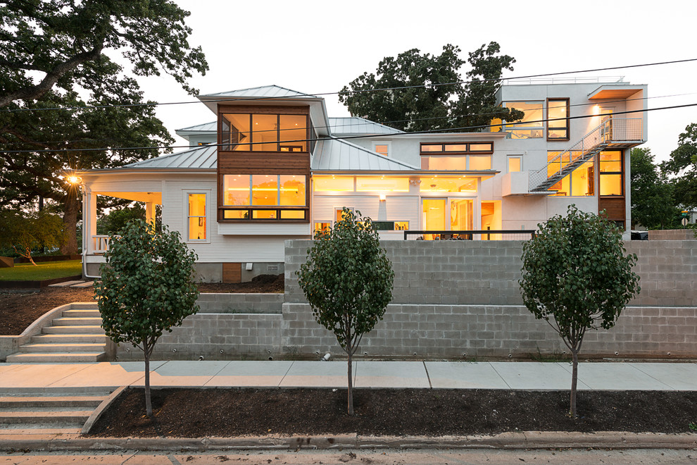 This is an example of a large contemporary split-level white house exterior in Austin with a hip roof, mixed siding and a metal roof.