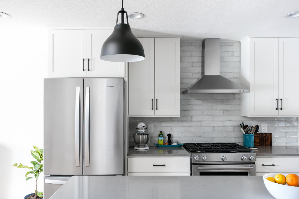 Mid-sized transitional l-shaped light wood floor and brown floor eat-in kitchen photo in Denver with an undermount sink, shaker cabinets, white cabinets, quartz countertops, white backsplash, porcelain backsplash, stainless steel appliances, an island and gray countertops