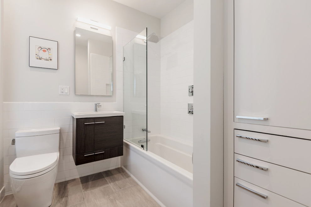 Mid-sized contemporary bathroom in Boston with flat-panel cabinets, dark wood cabinets, an alcove tub, a shower/bathtub combo, a one-piece toilet, white tile, subway tile, white walls, porcelain floors, an integrated sink, solid surface benchtops and an open shower.