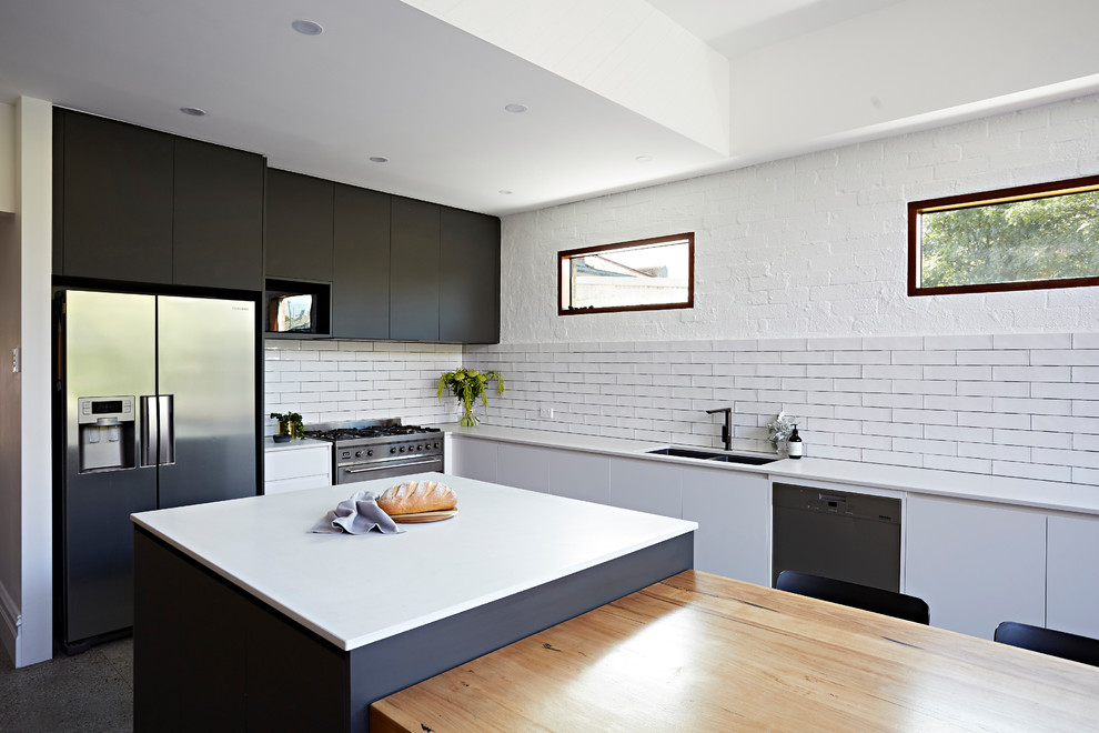 This is an example of a large contemporary u-shaped eat-in kitchen in Melbourne with an undermount sink, white splashback, stainless steel appliances, terrazzo floors, with island, multi-coloured floor, white benchtop, black cabinets, quartz benchtops and subway tile splashback.
