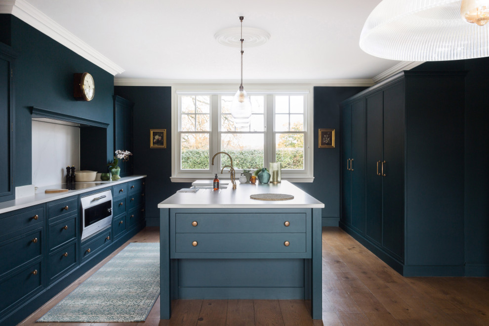 Inspiration for an expansive transitional u-shaped open plan kitchen in Kent with a farmhouse sink, shaker cabinets, quartzite benchtops, white splashback, limestone splashback, stainless steel appliances, with island, brown floor, white benchtop, blue cabinets and medium hardwood floors.