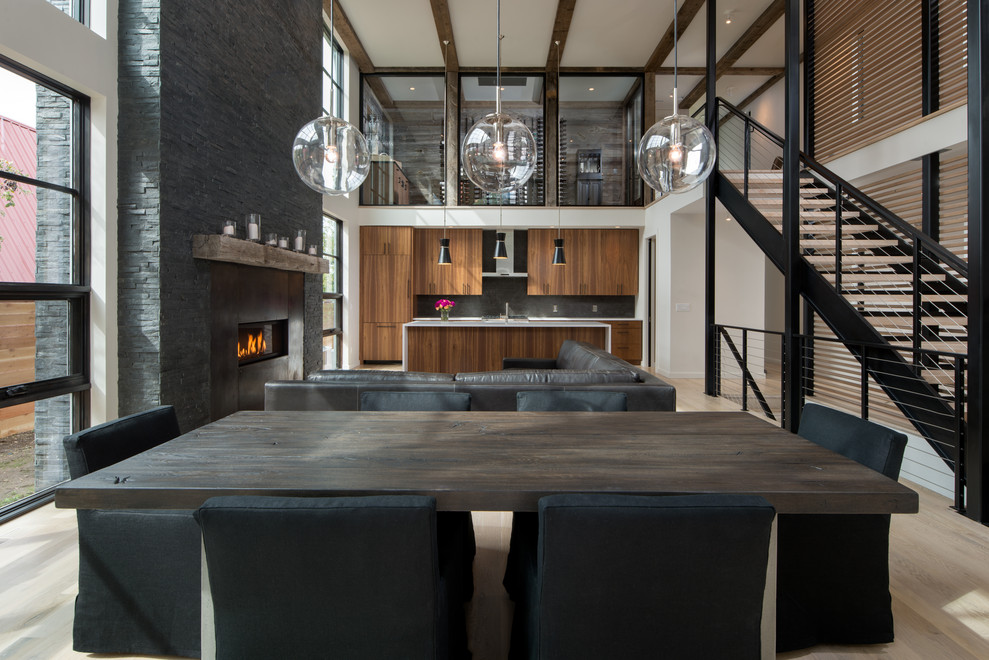 Mid-sized modern open plan dining in Other with grey walls, light hardwood floors, a standard fireplace, a metal fireplace surround and brown floor.