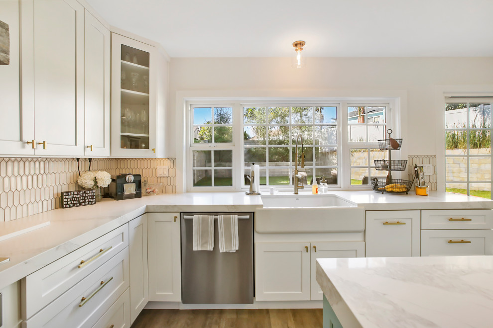 Expansive country u-shaped eat-in kitchen in Orange County with with island, a farmhouse sink, shaker cabinets, white cabinets, quartzite benchtops, white splashback, cement tile splashback, stainless steel appliances, medium hardwood floors, brown floor and white benchtop.