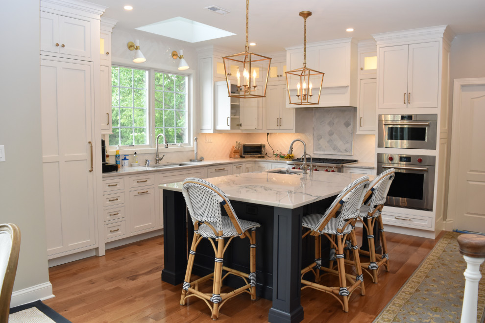 Design ideas for a large traditional l-shaped eat-in kitchen in Philadelphia with a farmhouse sink, recessed-panel cabinets, blue cabinets, quartzite benchtops, white splashback, porcelain splashback, panelled appliances, dark hardwood floors, with island, brown floor and blue benchtop.