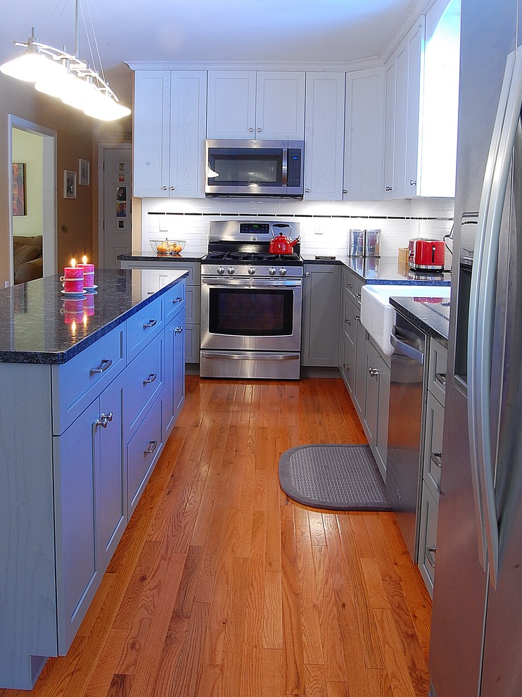 Inspiration for a mid-sized transitional l-shaped medium tone wood floor eat-in kitchen remodel in Boston with a farmhouse sink, shaker cabinets, white cabinets, quartz countertops, white backsplash, subway tile backsplash, stainless steel appliances and an island