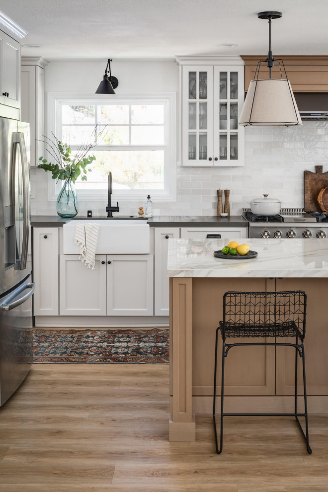 Large beach style l-shaped eat-in kitchen in San Diego with a farmhouse sink, shaker cabinets, light wood cabinets, solid surface benchtops, porcelain splashback, vinyl floors, with island and grey benchtop.